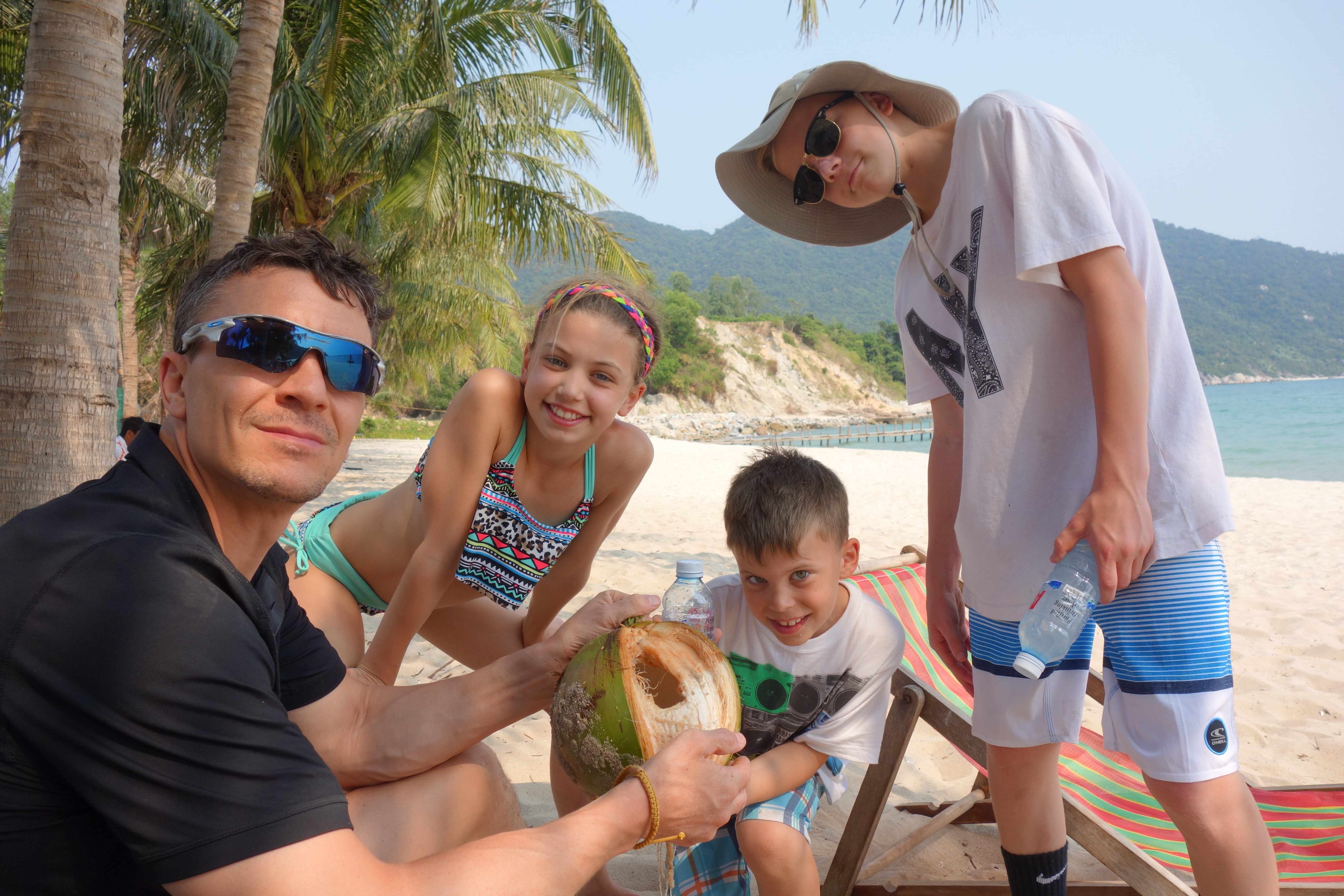 Philip and family on a beach in Asia drinking from a fresh coconut